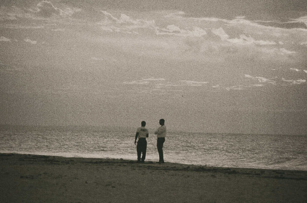 Two people standing quietly on a beach, facing the ocean, reflecting how to listen without trying to fix the pain.